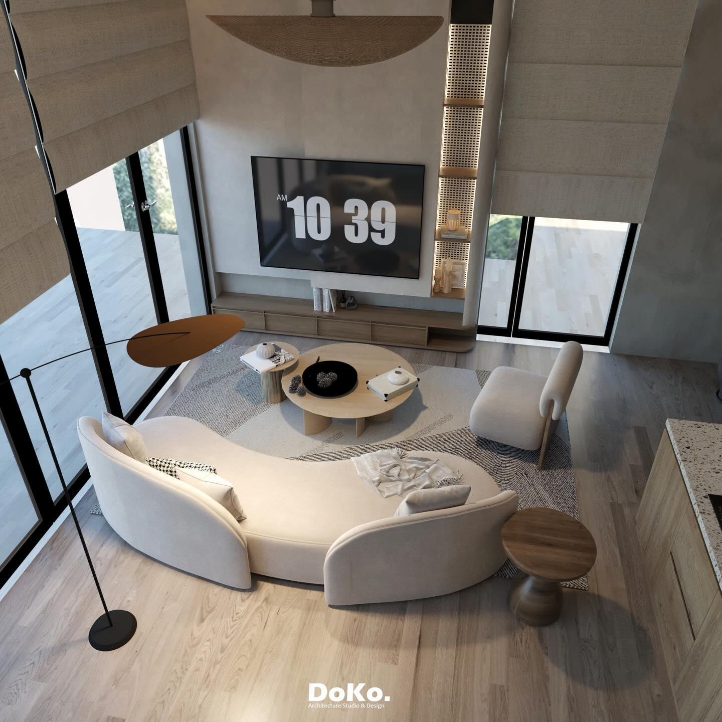 The beach villa living area from above: a curved white sofa, round timber tables, a floor lamp and roman blinds.