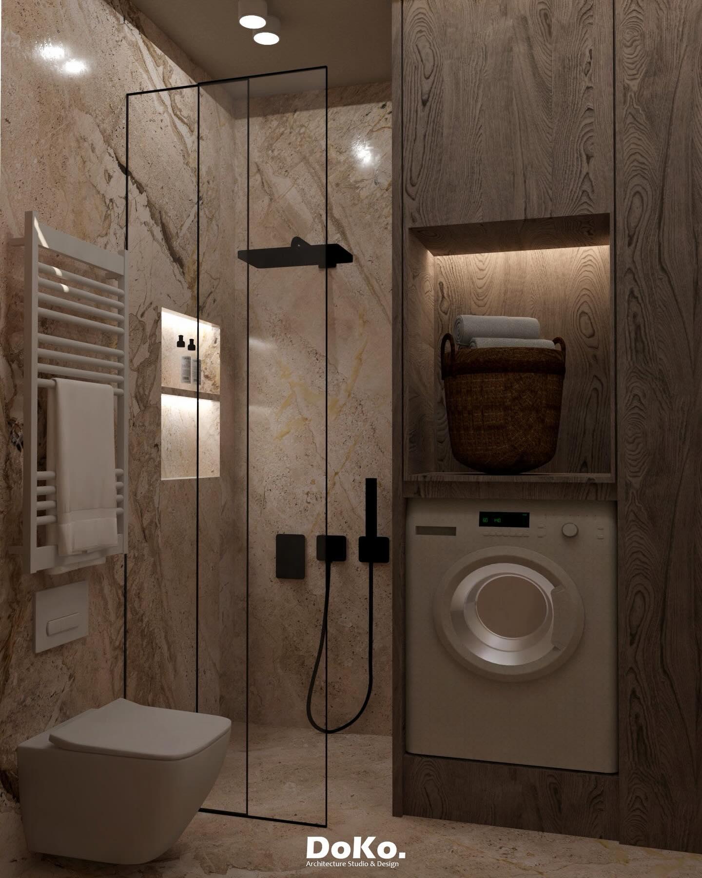 Compact bathroom in warm veined marble: glass shower, black fittings, a lit niche and a built-in washing machine.