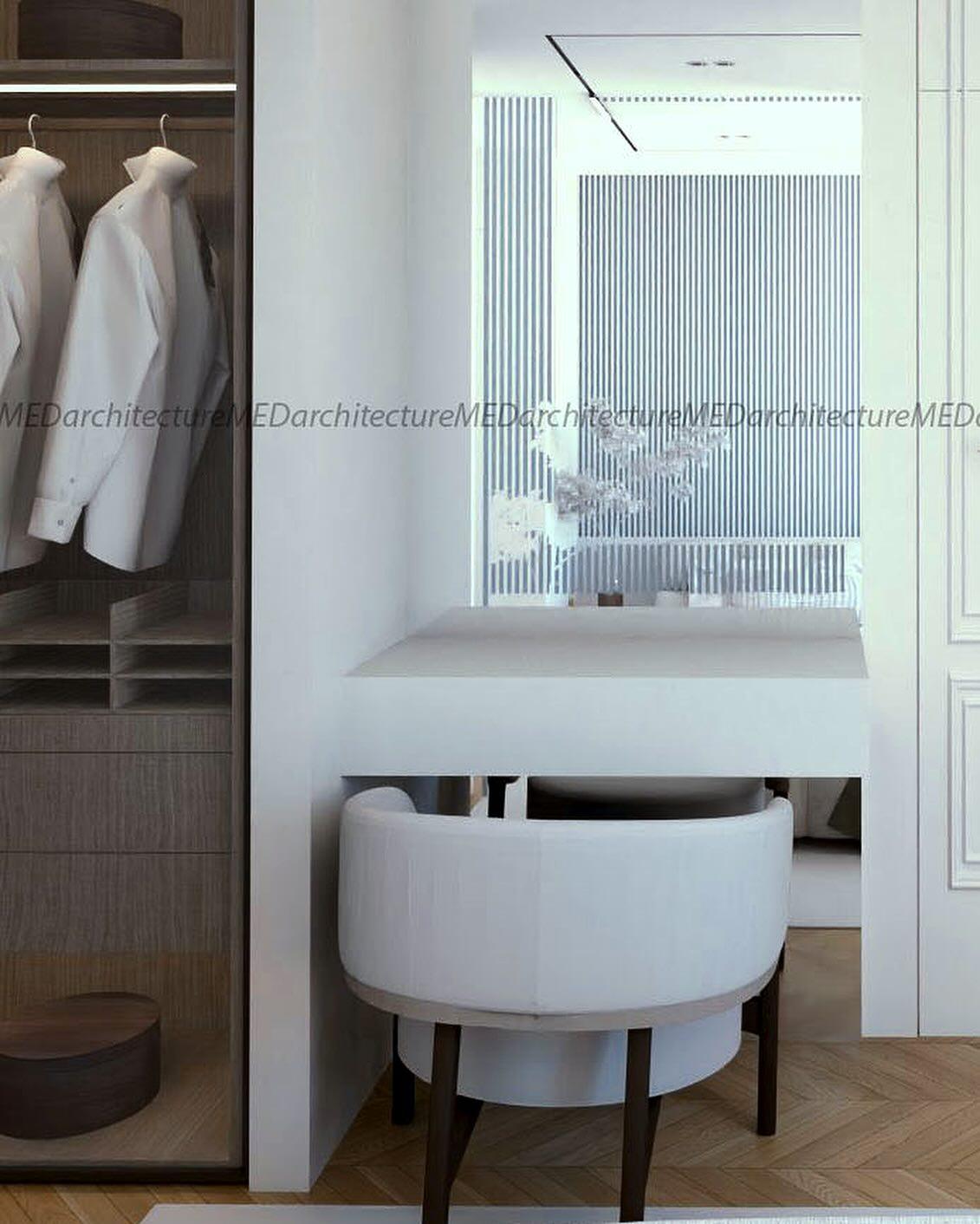 Dressing corner with a white vanity, a rounded upholstered chair and a glass-fronted wardrobe.