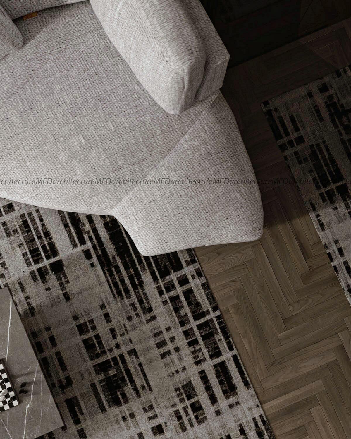 Top-down view of a grey armchair on a black-and-white rug and herringbone parquet.